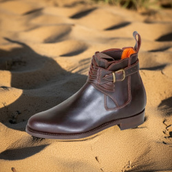 Spanische Reitstiefelette Cruzado braun, über dem Spann gekreuztes Leder seitliche Schnalle, schräge Seitansicht, auf Sand